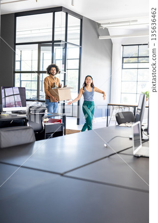 Colleagues carrying box and smiling while moving into modern office space Colleagues carrying box and smiling while moving into modern office space 135636462