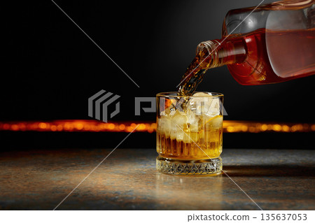 Whiskey is poured into a glass with ice. Whiskey is poured into a glass with ice. 135637053
