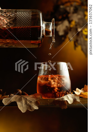 Whiskey is poured into a glass with ice. Whiskey is poured into a glass with ice. 135637062