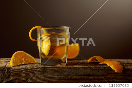 Old Fashioned cocktail with a ice, garnished with an orange peel on a old wooden board. 135637083