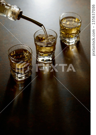 Whiskey pour from a bottle into a small glasses. 135637086