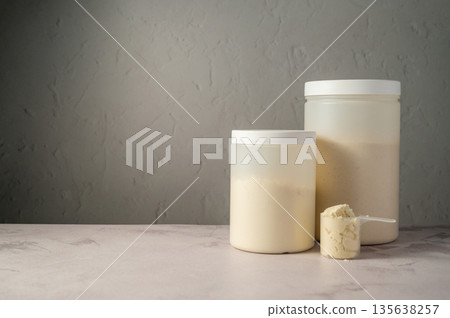 Protein powder in scoops with white plastic protein tubes, jars in background. Body building, muscle growth and food supplement concept 135638257