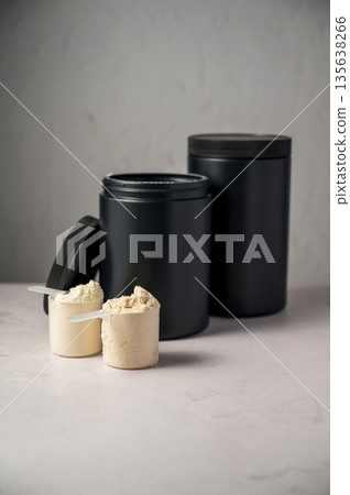 Protein powder in scoops with black protein tubes, jars in background. Body building, muscle growth and food supplement concept 135638266