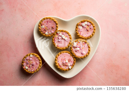 Valentine's day dessert. Pink mini tarts with heart shaped sprinkles in heart plate. Top view, copy space 135638280