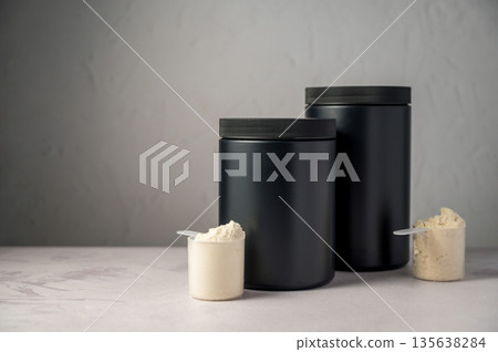 Protein powder in scoops with black protein tubes, jars in background. Body building, muscle growth and food supplement concept 135638284