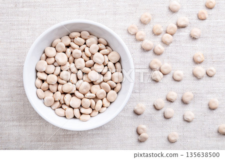 Sweet lupin beans, in white bowl on linen. Dried seeds of white lupin, Lupinus albus, a special cultivar, low in toxic and bitter-tasting alkaloids, and high in protein, used as meat substitute. Photo 135638500