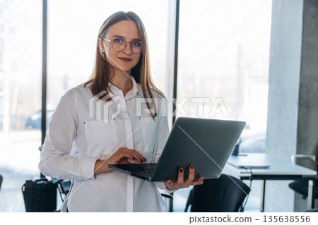 Laptop is in hands. Businesswoman, coach is standing in conference room Laptop is in hands. Businesswoman, coach is standing in conference room 135638556