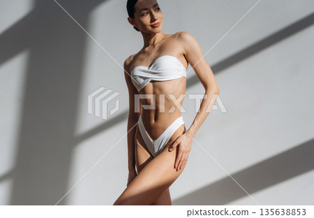White clothes, bikini. Beautiful young woman with slim body type is indoors White clothes, bikini. Beautiful young woman with slim body type is indoors 135638853
