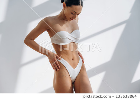 Showing abs, standing. Beautiful young woman with slim body type is indoors Showing abs, standing. Beautiful young woman with slim body type is indoors 135638864