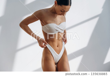 Showing abs, standing. Beautiful young woman with slim body type is indoors Showing abs, standing. Beautiful young woman with slim body type is indoors 135638865