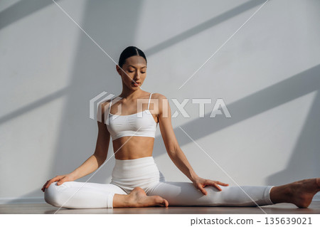 On the floor, doing yoga sport exercises. Beautiful young woman with slim body type is indoors On the floor, doing yoga sport exercises. Beautiful young woman with slim body type is indoors 135639021