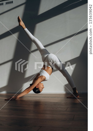 Legs are stretching, yoga exercise. Beautiful young woman with slim body type is indoors Legs are stretching, yoga exercise. Beautiful young woman with slim body type is indoors 135639042