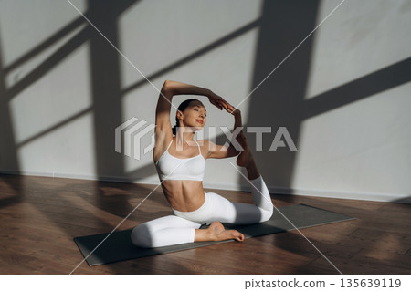 Health care, physical activity, sitting on the floor. Beautiful young woman with slim body type is indoors Health care, physical activity, sitting on the floor. Beautiful young woman with slim body type is indoors 135639119