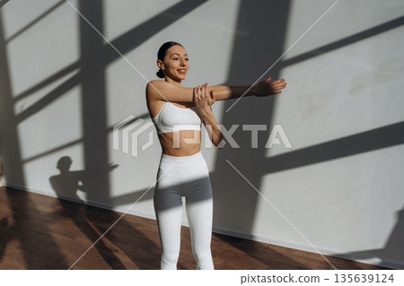 Warm up exercise. Beautiful young woman with slim body type is indoors Warm up exercise. Beautiful young woman with slim body type is indoors 135639124