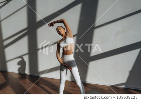 Warm up exercise. Beautiful young woman with slim body type is indoors Warm up exercise. Beautiful young woman with slim body type is indoors 135639125