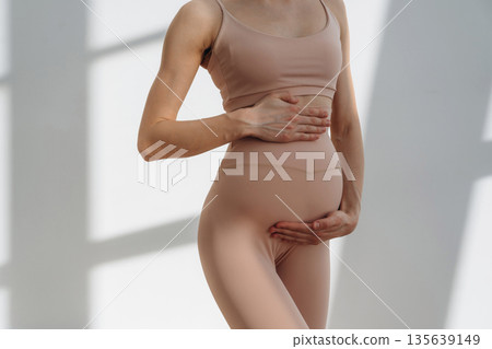 Touching the abdomen. Pregnant woman is indoors Touching the abdomen. Pregnant woman is indoors 135639149
