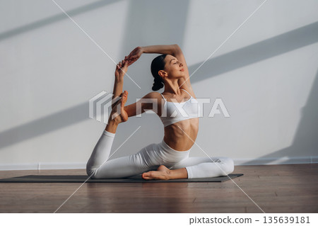 Enjoying doing yoga. Beautiful young woman with slim body type is indoors Enjoying doing yoga. Beautiful young woman with slim body type is indoors 135639181