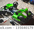 Green go-kart parked on sunlit brick pavement. 135640179