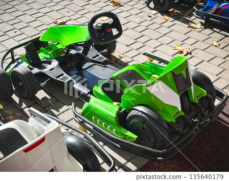 Green go-kart parked on sunlit brick pavement. 135640179