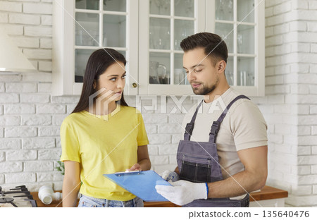 Repairman in uniform giving woman client contract for repair to sign after finished work 135640476