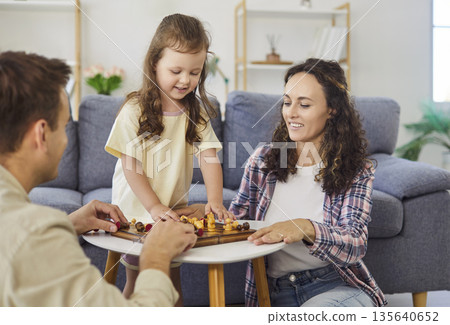 Happy family learning rules of chess together at home, parents teach daughter Happy family learning rules of chess together at home, parents teach daughter 135640652