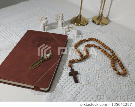 Catholic corner at home. Angel figurine, wooden rosary beads, cross, and prayer book. Faith, symbols, and traditions. Catholic corner at home. Angel figurine, wooden rosary beads, cross, and prayer book. Faith, symbols, and traditions. 135641297