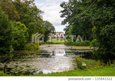 Historic mansion reflected in calm pond at Park Rams Woerthe in Netherlands surrounded by green trees 135641522
