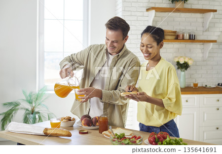 Couple cooking breakfast together at home kitchen, man pouring juice to glass Couple cooking breakfast together at home kitchen, man pouring juice to glass 135641691