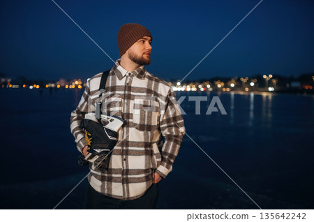 Standing and looking far away. A man is on the ice with his skates in winter Standing and looking far away. A man is on the ice with his skates in winter 135642242