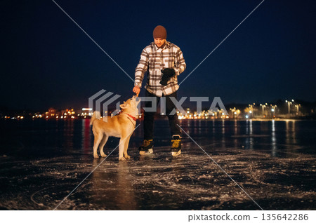 Together on the frozen lake. Man with Akita Inu dog is on the ice with skates in winter Together on the frozen lake. Man with Akita Inu dog is on the ice with skates in winter 135642286