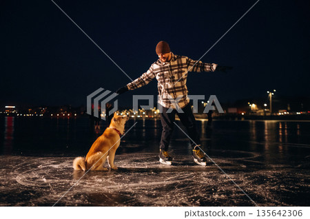 Around the pet, riding. Man with Akita Inu dog is on the ice with skates in winter 135642306