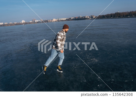 Riding on the frozen lake. A man is on the ice with his skates in winter Riding on the frozen lake. A man is on the ice with his skates in winter 135642308