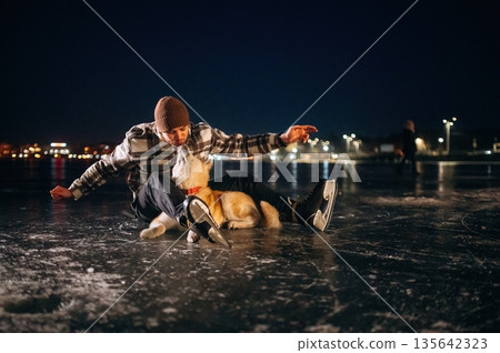 Night time. Man with Akita Inu dog is on the ice with skates in winter Night time. Man with Akita Inu dog is on the ice with skates in winter 135642323