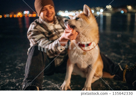 Lovely moments with cute pet. Man with Akita Inu dog is on the ice with skates in winter Lovely moments with cute pet. Man with Akita Inu dog is on the ice with skates in winter 135642330