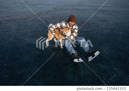 Lovely moments with cute pet. Man with Akita Inu dog is on the ice with skates in winter 135642333