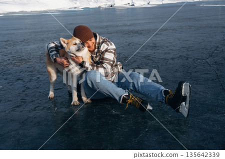 Smiling, embracing the pet. Man with Akita Inu dog is on the ice with skates in winter 135642339