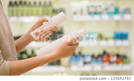 Woman compares and chooses hair care products in the store, carefully examining and reading option labels to make an informed purchasing decision. Woman compares and chooses hair care products in the store, carefully examining and reading option labels to make an informed purchasing decision. 135642793