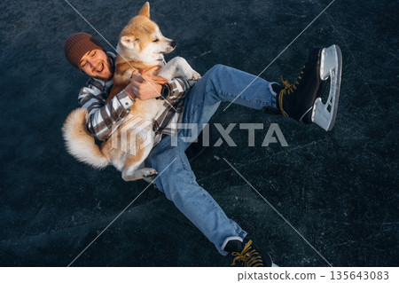 Smiling, embracing the pet. Man with Akita Inu dog is on the ice with skates in winter Smiling, embracing the pet. Man with Akita Inu dog is on the ice with skates in winter 135643083