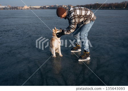 Human's best friend. Man with Akita Inu dog is on the ice with skates in winter Human's best friend. Man with Akita Inu dog is on the ice with skates in winter 135643093