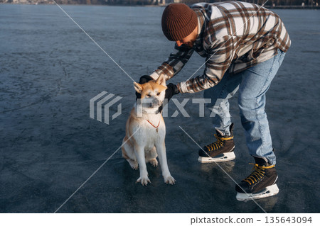 Human's best friend. Man with Akita Inu dog is on the ice with skates in winter Human's best friend. Man with Akita Inu dog is on the ice with skates in winter 135643094