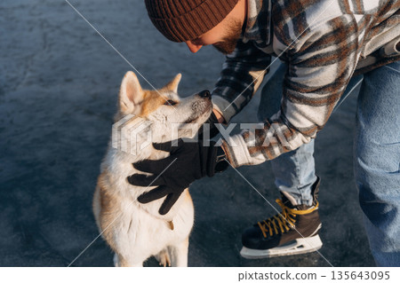 Human's best friend. Man with Akita Inu dog is on the ice with skates in winter 135643095