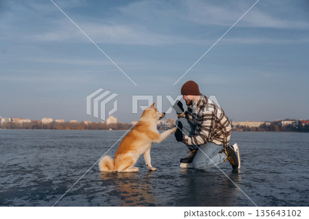 Training the tricks, giving paw. Man with Akita Inu dog is on the ice with skates in winter 135643102