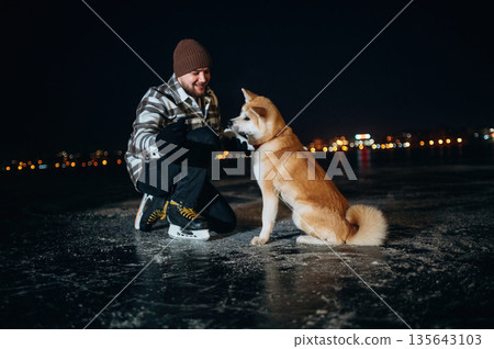Man with Akita Inu dog is on the ice with skates in winter Man with Akita Inu dog is on the ice with skates in winter 135643103