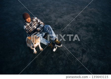Dark ice, top view. Man with Akita Inu dog is on the ice with skates in winter Dark ice, top view. Man with Akita Inu dog is on the ice with skates in winter 135643115