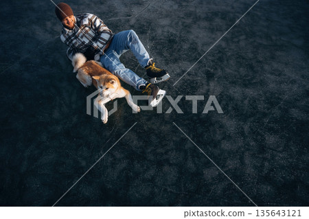 View from the top, lying down. Man with Akita Inu dog is on the ice with skates in winter View from the top, lying down. Man with Akita Inu dog is on the ice with skates in winter 135643121