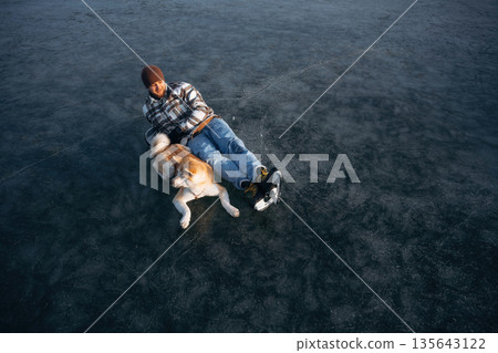 View from the top, lying down. Man with Akita Inu dog is on the ice with skates in winter 135643122