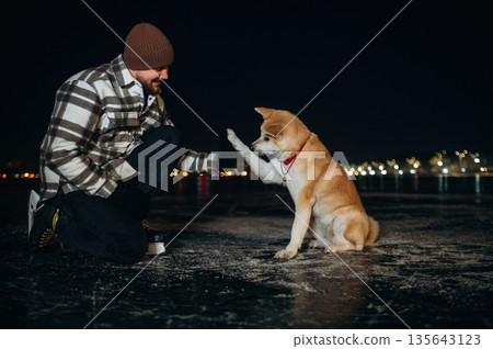 Giving the paw. Man with Akita Inu dog is on the ice with skates in winter Giving the paw. Man with Akita Inu dog is on the ice with skates in winter 135643123