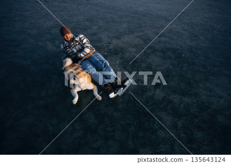View from the top, lying down. Man with Akita Inu dog is on the ice with skates in winter View from the top, lying down. Man with Akita Inu dog is on the ice with skates in winter 135643124