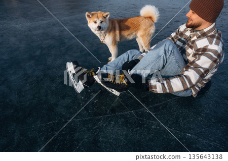 Top view, sitting. Man with Akita Inu dog is on the ice with skates in winter 135643138