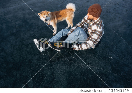 Top view, sitting. Man with Akita Inu dog is on the ice with skates in winter 135643139